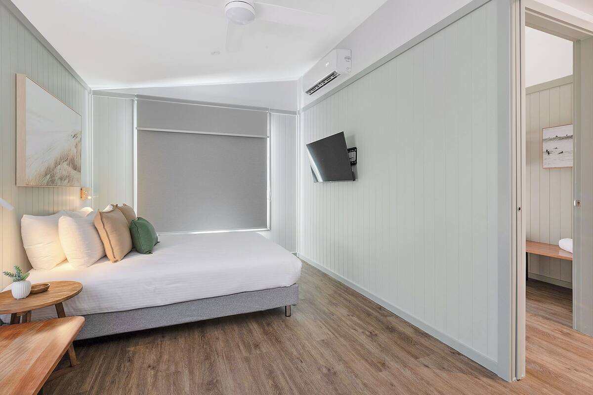A bedroom with a bed, bedside table, and a wall-mounted TV.