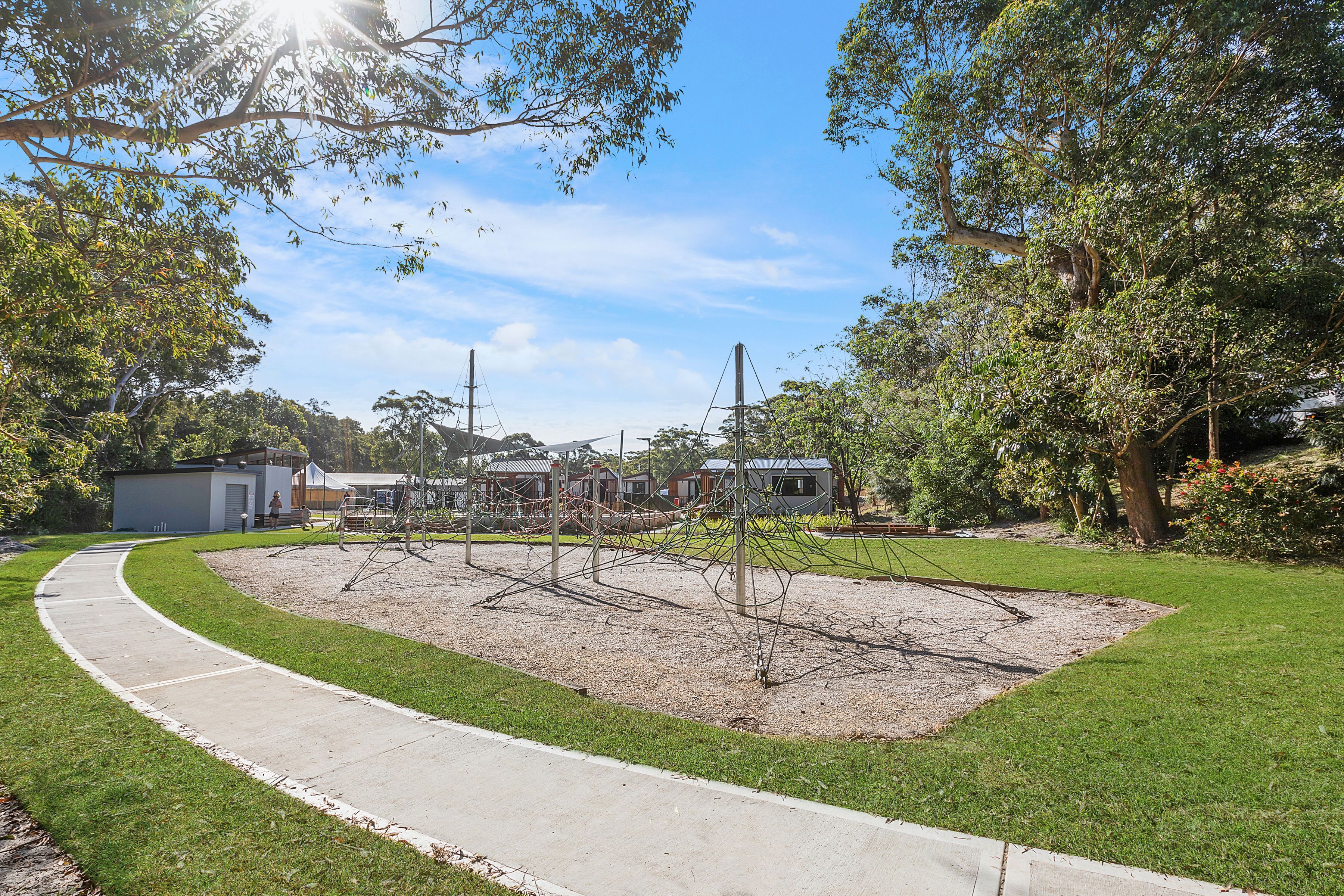 A park with a paved walkway, playground equipment, and a grassy area.