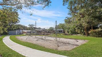 A park with a paved walkway, playground equipment, and a grassy area.