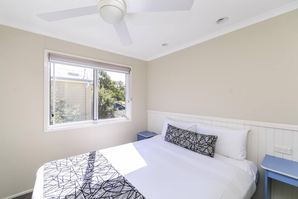 A bedroom with a bed, a window, a ceiling fan, and a nightstand.