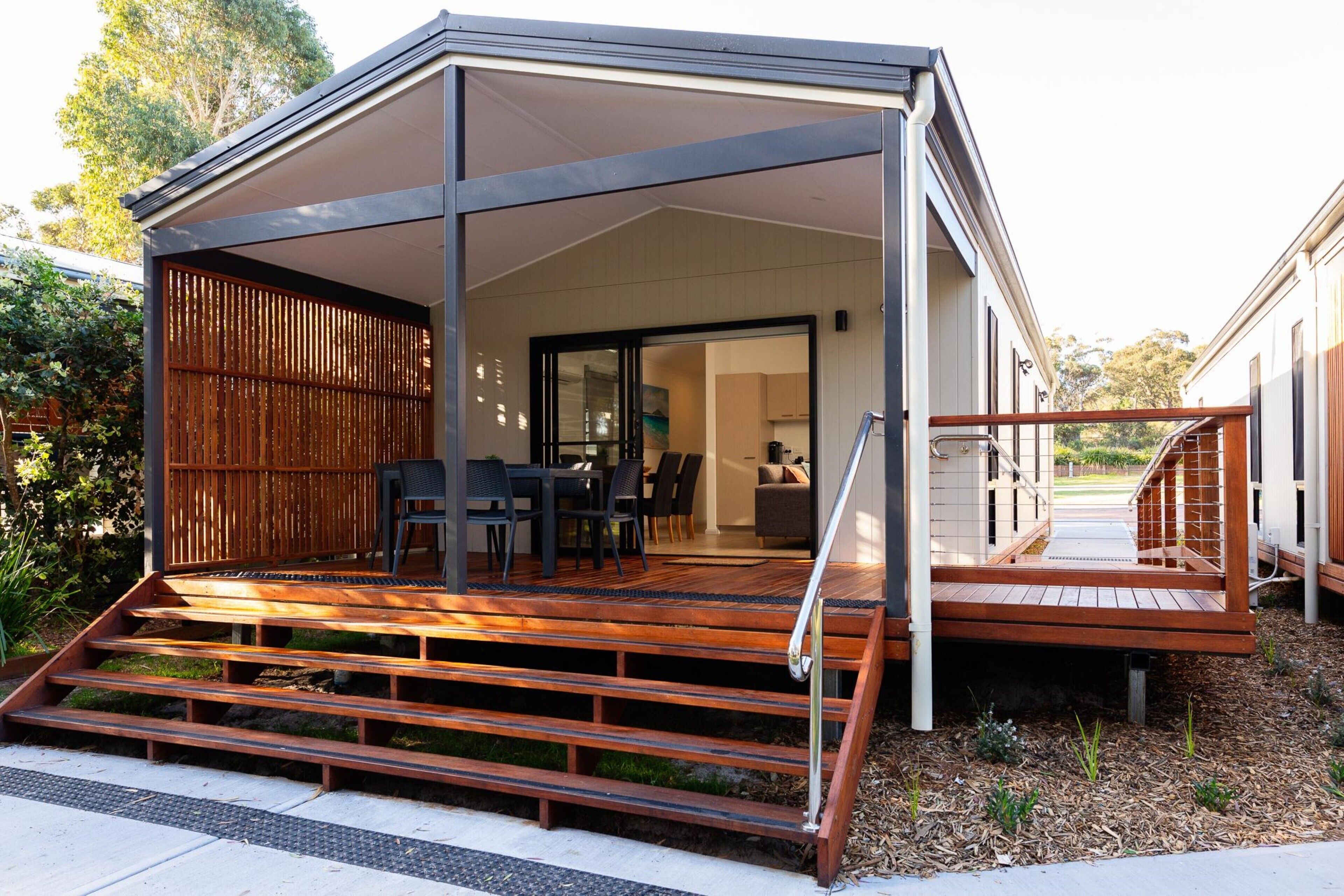 A modern house with a covered outdoor area, a wooden deck, and a staircase leading to a glass door entrance.