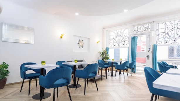 Un comedor moderno con sillas azules y mesas blancas, que incluye una puerta metálica decorativa y una planta en maceta.