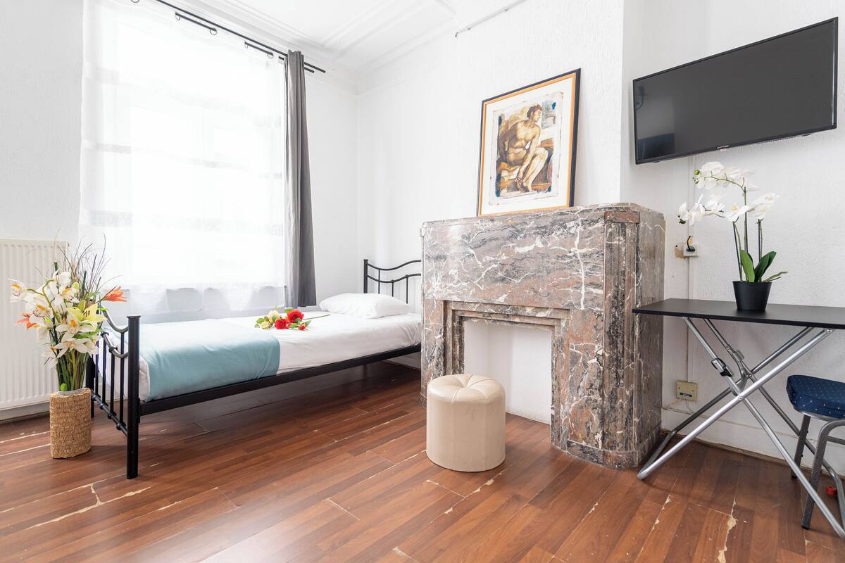 A bedroom with a bed, a stone fireplace, a TV mounted on the wall, and a potted orchid.