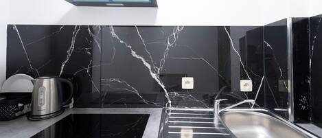 Una cocina moderna con salpicadero de mármol negro, pileta de acero inoxidable y una tetera sobre la encimera.