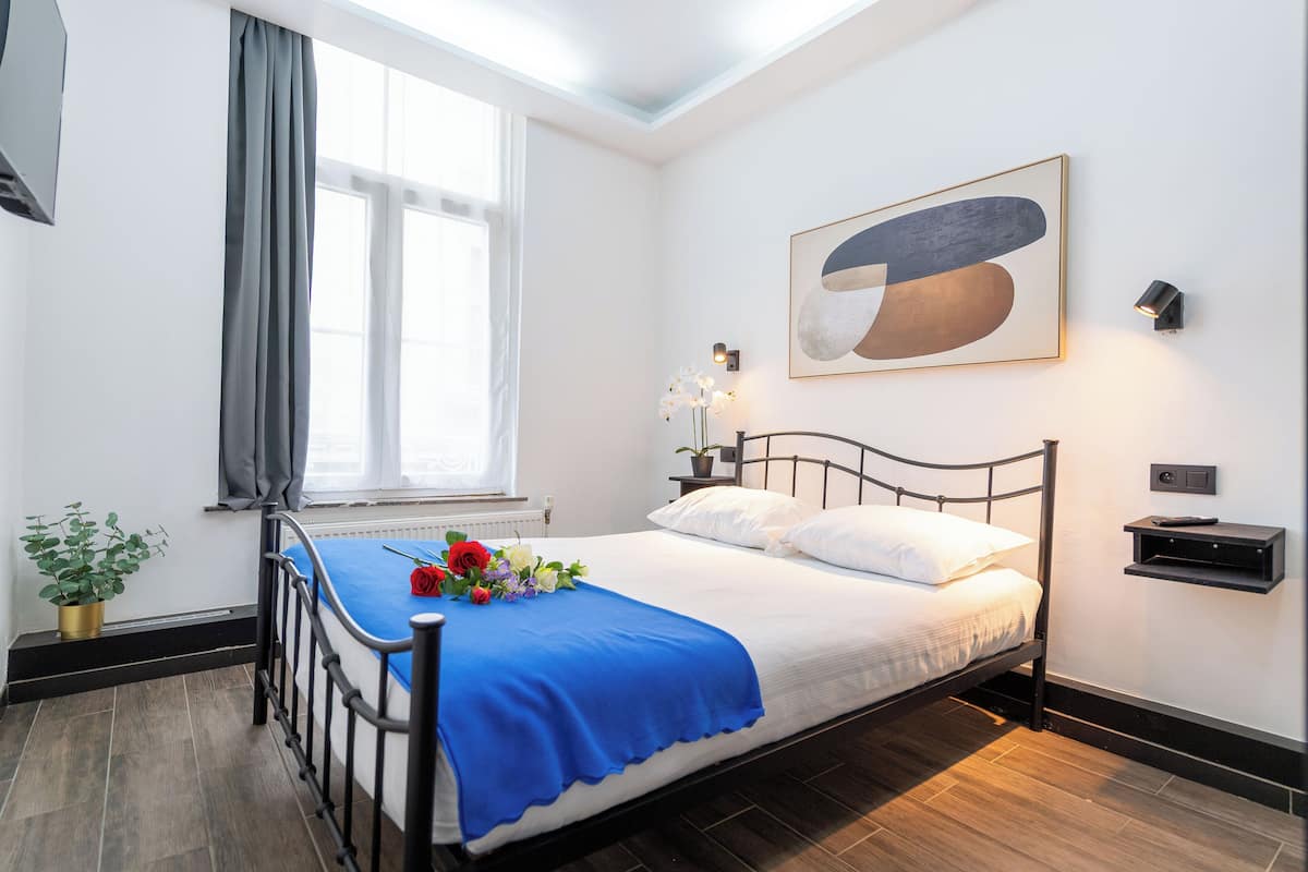 A neatly made bed with a blue bedspread, a potted plant, and a wall-mounted shelf.