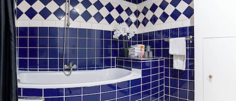 A bathroom with a large bathtub, blue and white tiles, a shower, and a toilet.