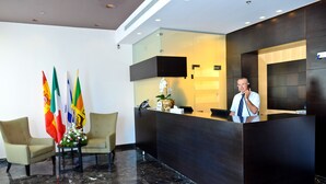 A reception area with a dark reception desk, beige chairs, and multiple flags. - Golden Crown Old City Hotel (Nazareth)