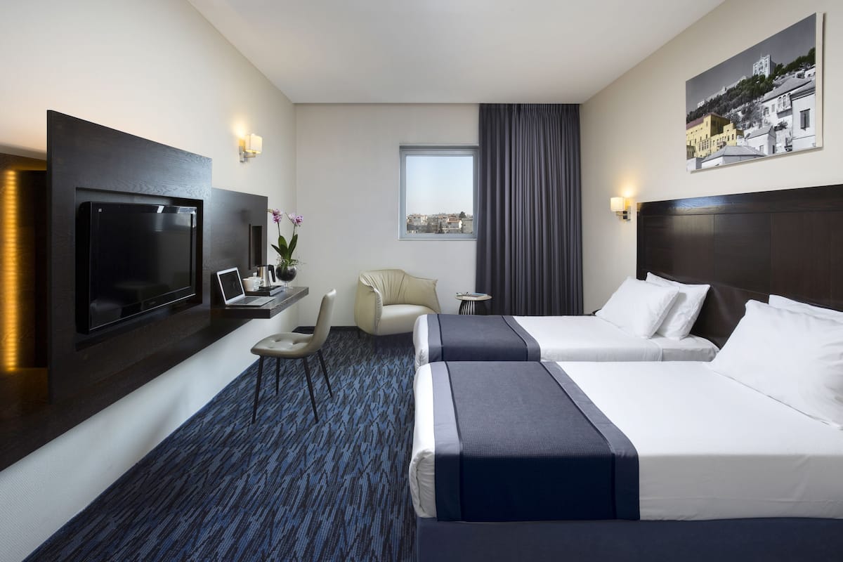 Une chambre d’hôtel avec deux lits, un téléviseur à écran plat, un bureau avec une chaise, une petite table et une fenêtre donnant sur des immeubles.