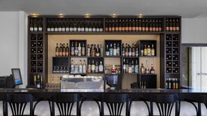A bar area with multiple shelves of bottles and glasses, a counter with a cash register, and black bar stools. - Golden Crown Old City Hotel (Nazareth)