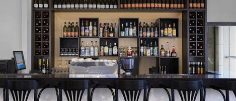 A bar area with multiple shelves of bottles and glasses, a counter with a cash register, and black bar stools.