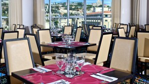 A restaurant with tables set for dining, large windows offering a city view, and a modern interior design. - Golden Crown Old City Hotel (Nazareth)