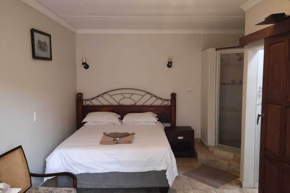 A bedroom with a single bed, a nightstand, a chair, and a door leading to a bathroom.