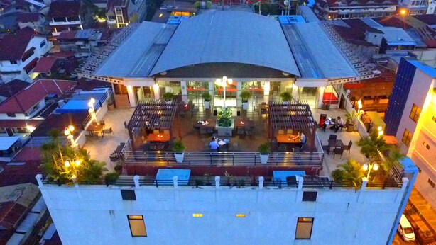 Un edificio alto con terraza en la azotea, que cuenta con asientos al aire libre y un área de comedor central.