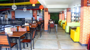 Un restaurante con varias mesas y sillas, pilares de ladrillo y faroles colgantes.