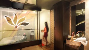 Un baño moderno con cabina de ducha de vidrio, un banco de madera y un tocador con un cesto de artículos de aseo.