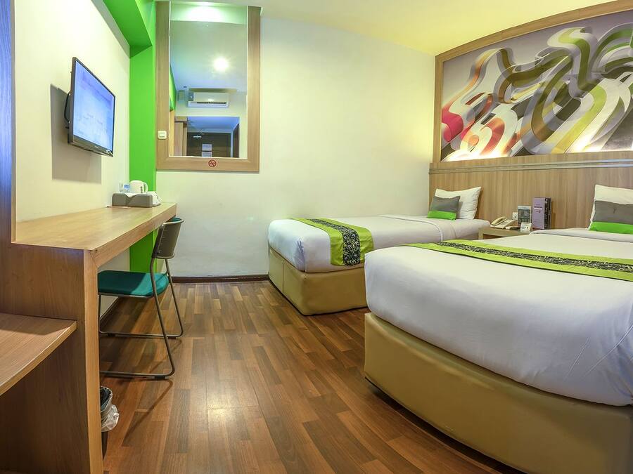 A hotel room with a desk, two beds, a green wall, and a large abstract painting.
