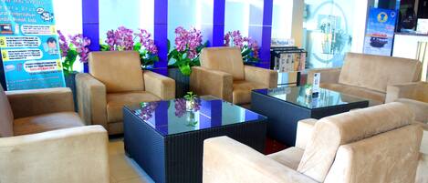A lobby with beige sofas, a glass-top coffee table, and purple orchids.