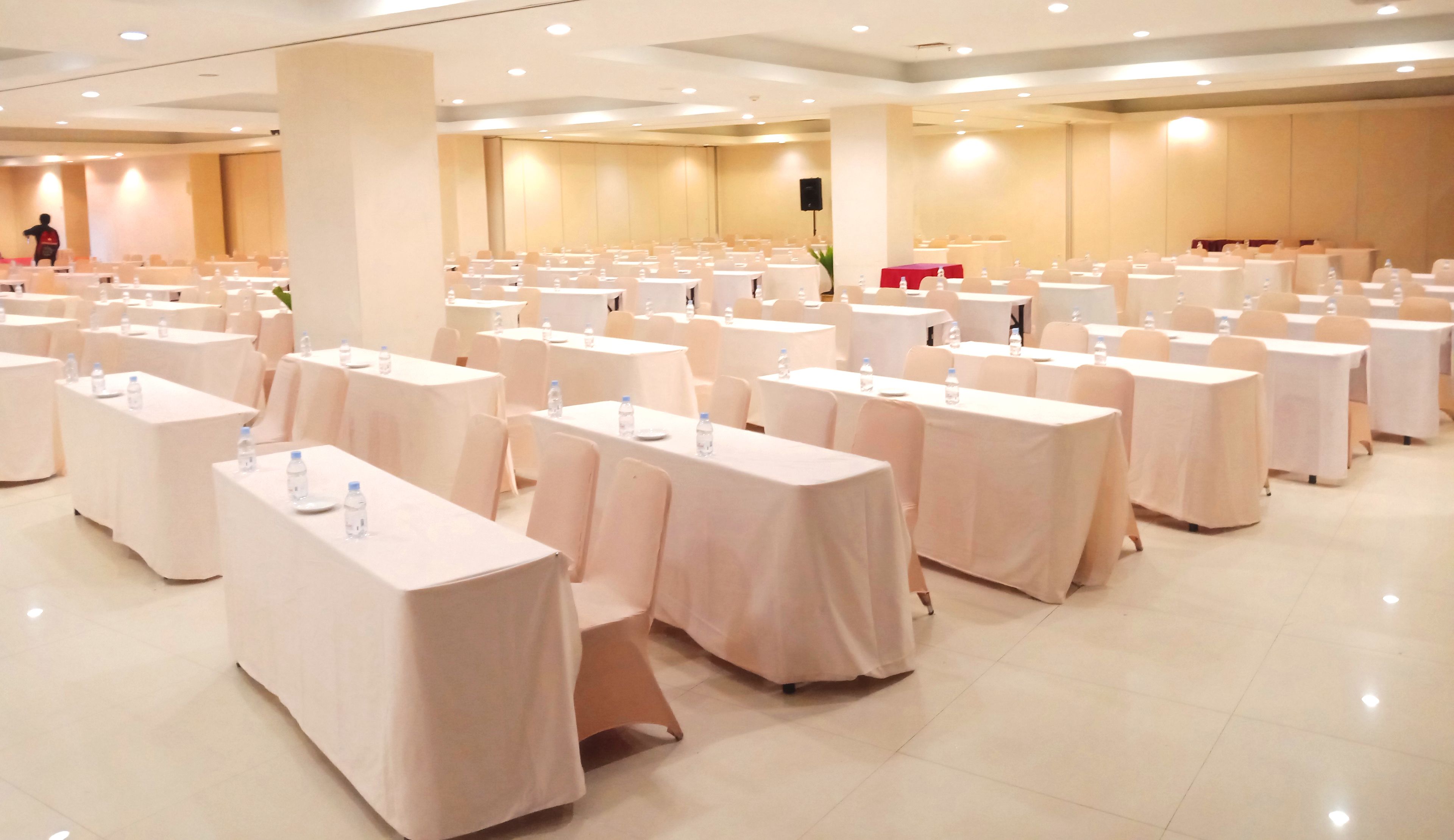 Une salle de conférence avec des rangées de tables, chacune étant équipée d’une bouteille d’eau et d’une assiette.