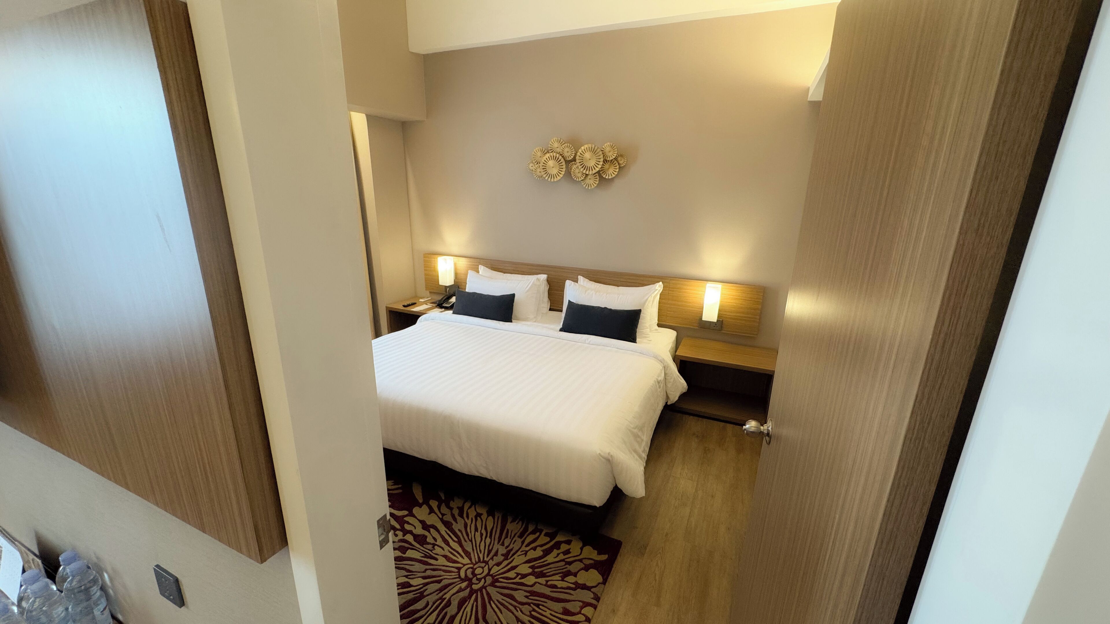 A hotel room with a large bed, bedside tables, a wall-mounted light fixture, and a decorative wall piece.