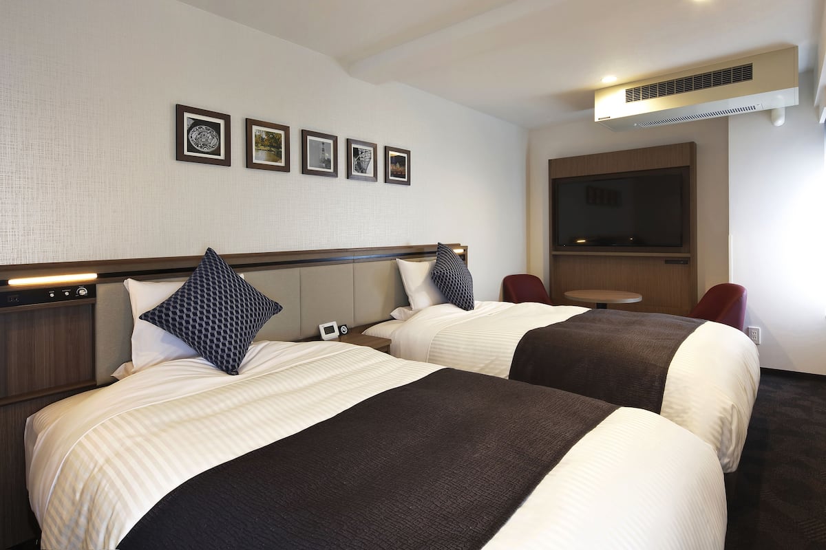 A hotel room with two beds, a TV, a small table, and a chair.