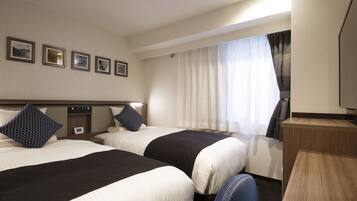 A hotel room with two beds, a desk, a TV, and a window with curtains.