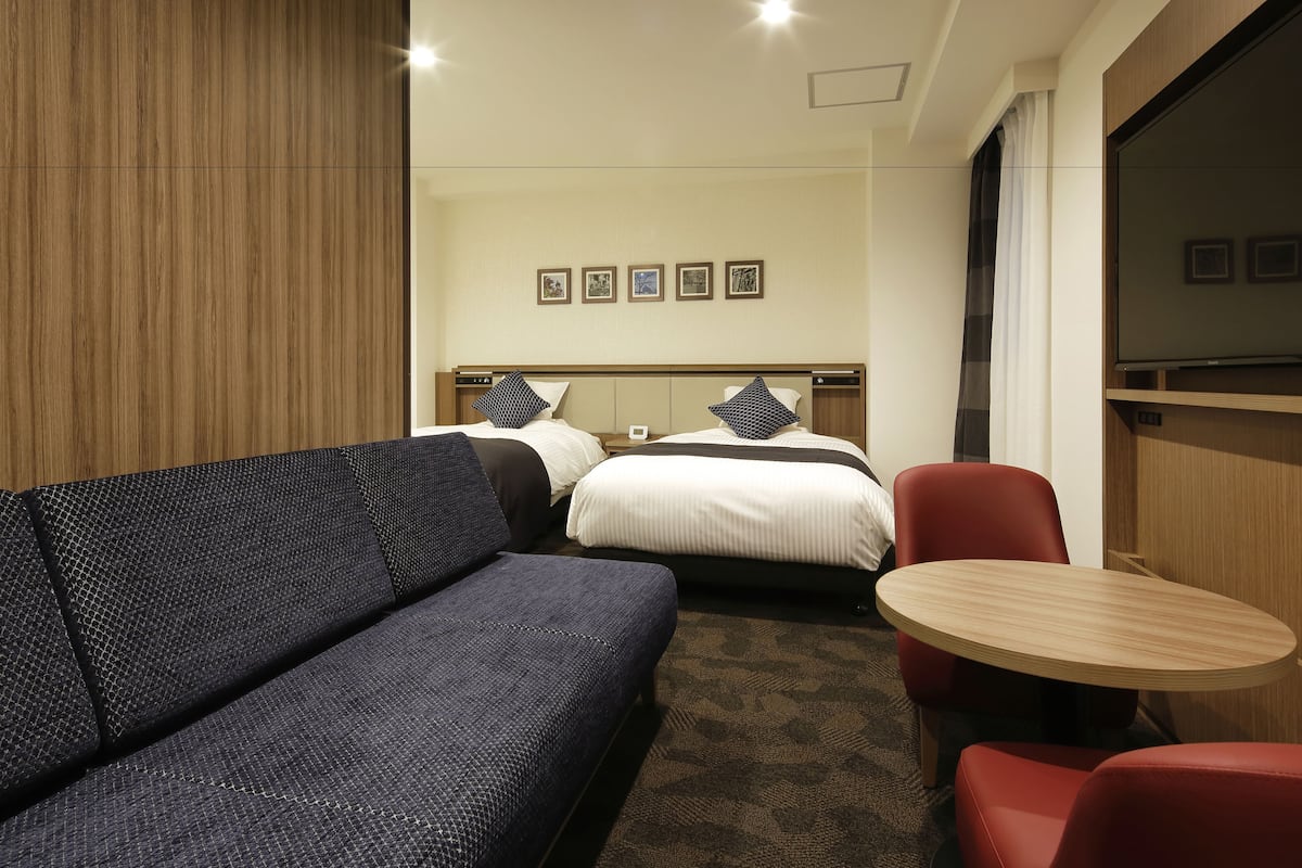 A hotel room with a bed, a sofa, a small table, and a TV.