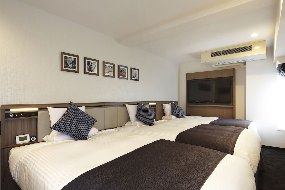 A hotel room with two beds, a flat-screen TV mounted on the wall, and a digital clock on the nightstand.