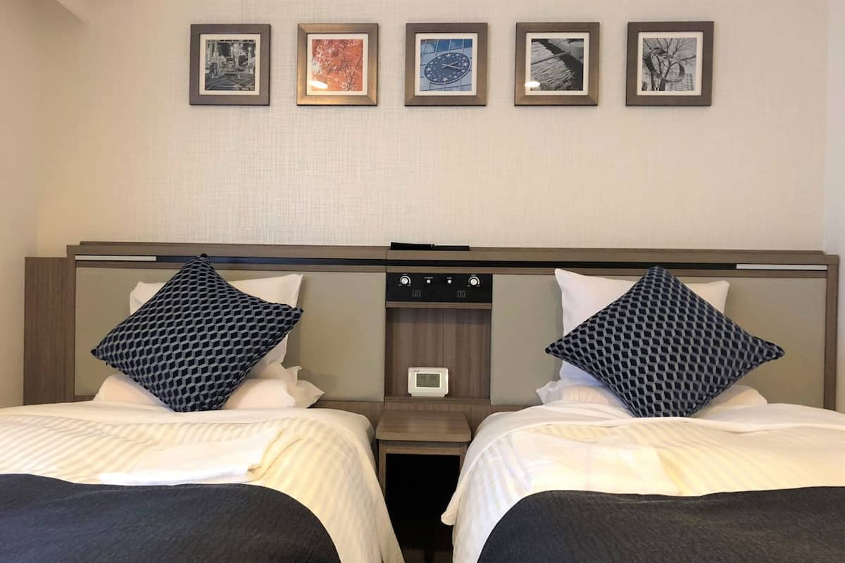 A hotel room with two beds, a nightstand, a digital clock, and four framed pictures on the wall.