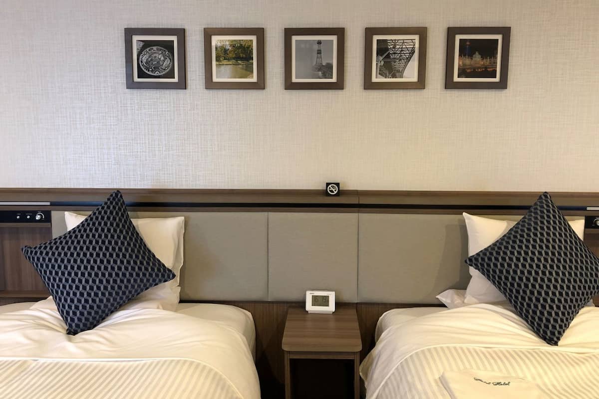 A hotel room with two beds, a headboard, a nightstand, and five framed pictures on the wall.