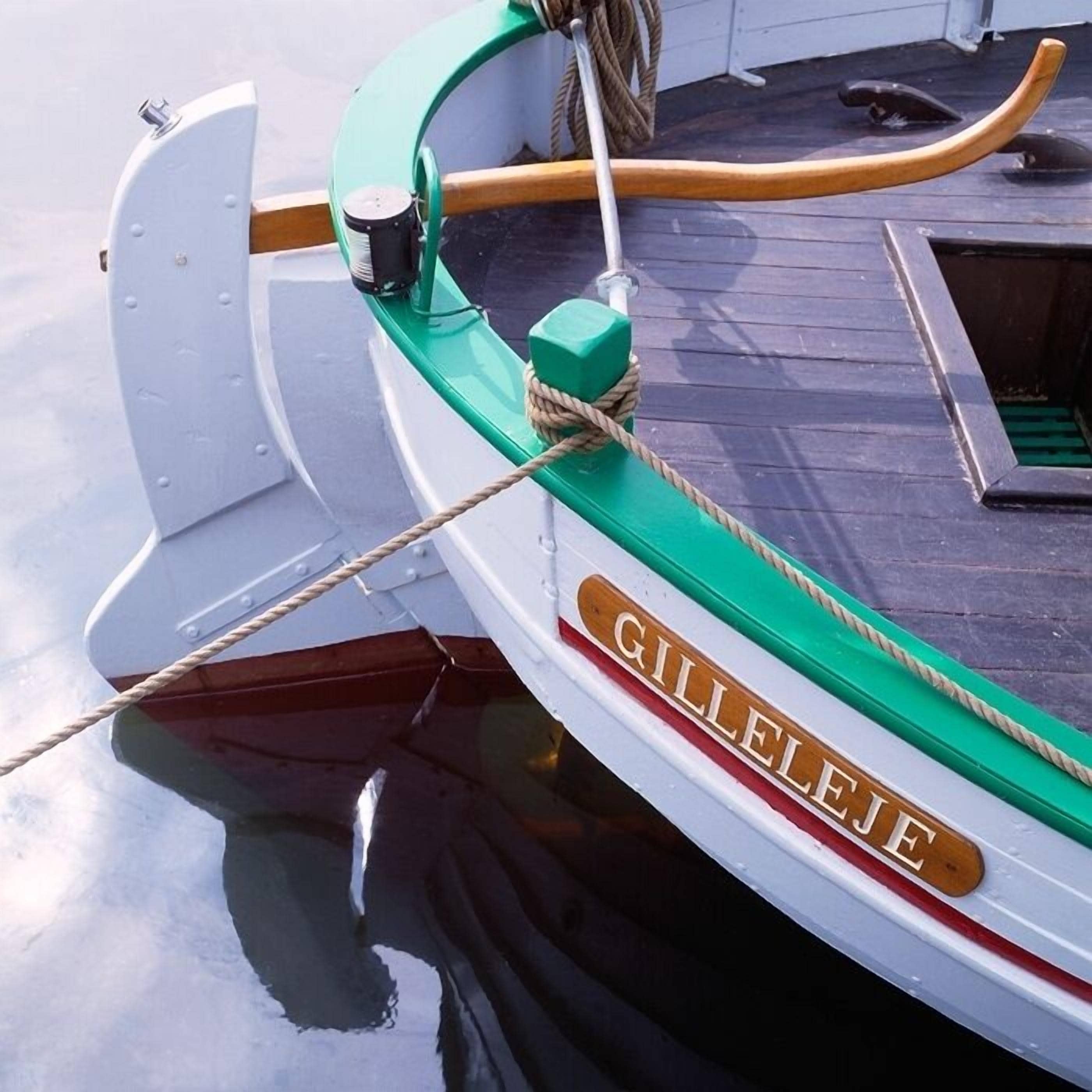 A boat named GILLEJE with a green and white color scheme, a rope tied to a cleat, and a metal cleat on the side.