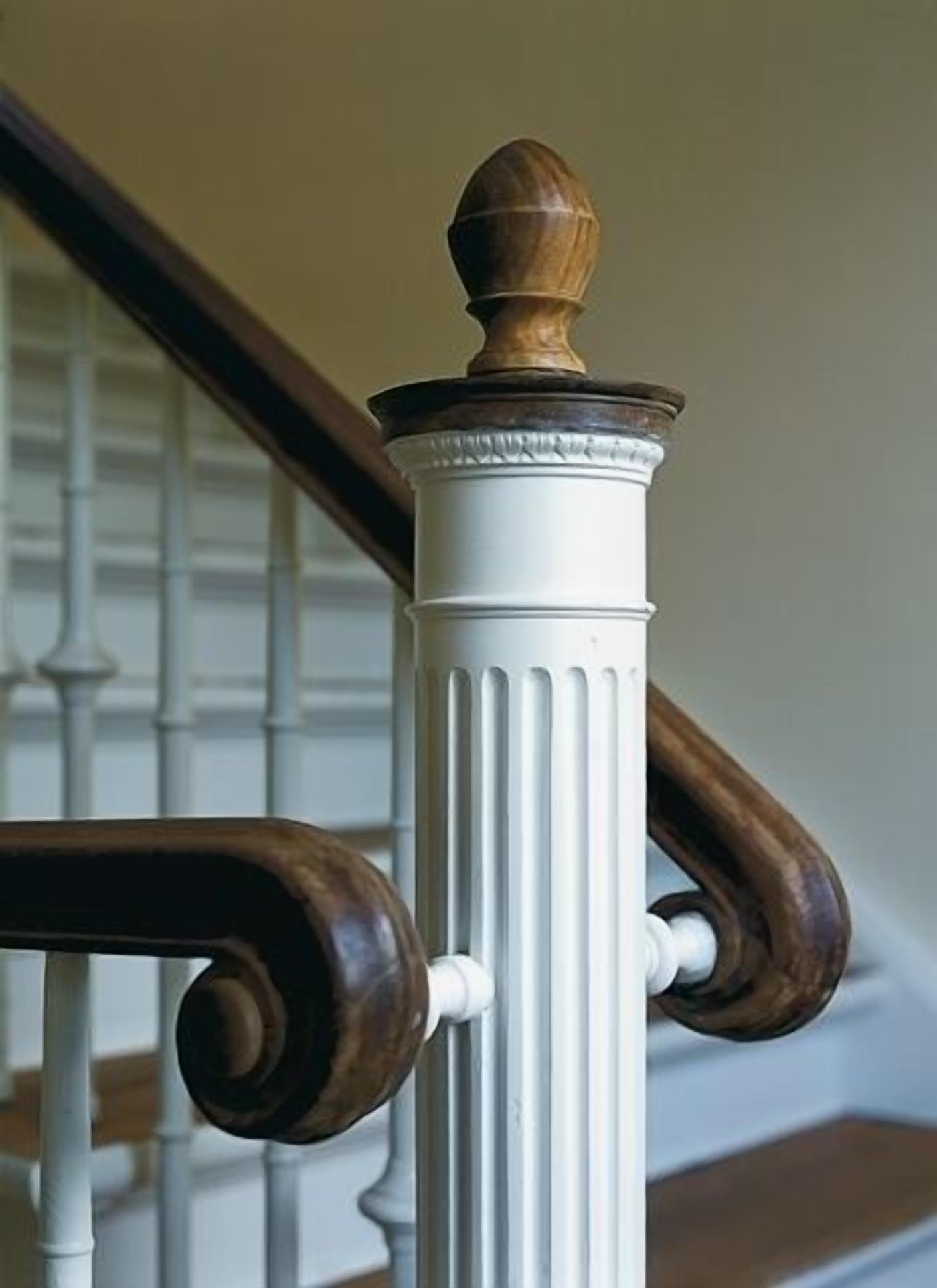 A white column with a wooden finial and a curved wooden handrail.