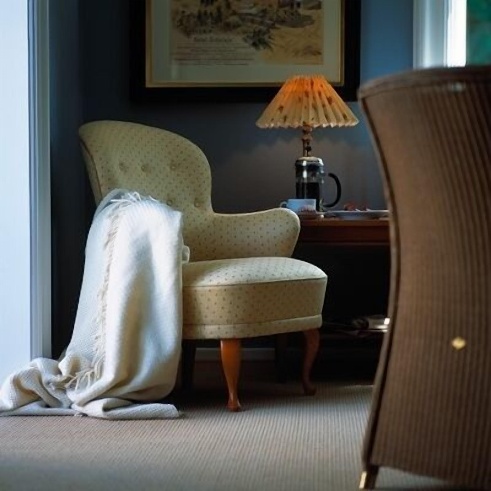Una habitación con un sillón estampado, una mesita con una lámpara y un cuadro en la pared.