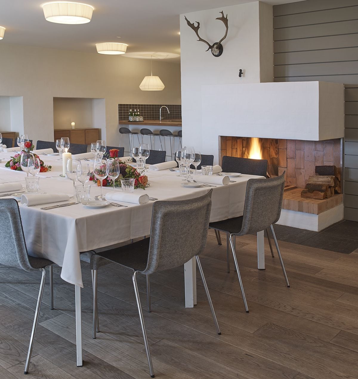 Uma sala de jantar com uma mesa comprida posta para refeição, cadeiras modernas e uma lareira com lenha acesa.