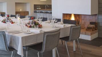 A dining area with a long table set for a meal, modern chairs, and a fireplace with a log fire.