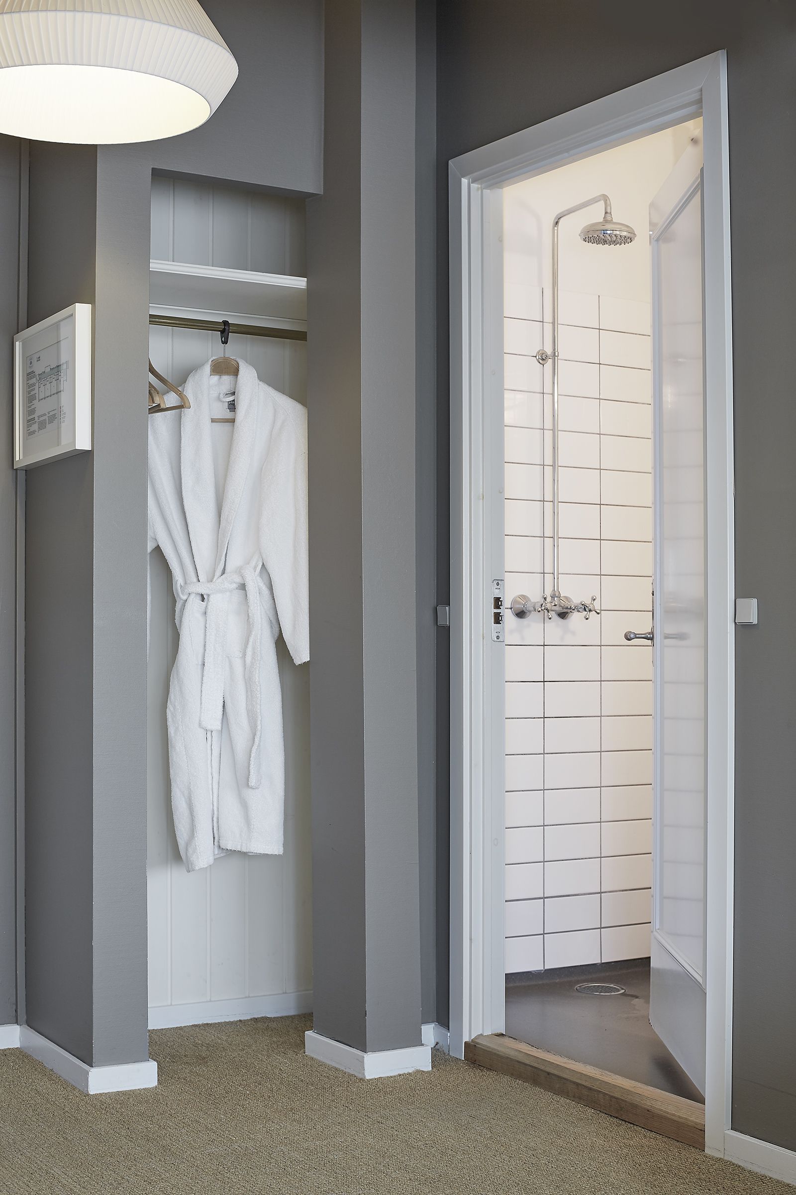 A bathroom with a shower, a towel rack with a white bathrobe, and a framed picture on the wall.