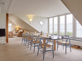 Una habitación amplia con techo alto, una gran mesa de comedor rodeada de sillas, un sofá y un televisor.