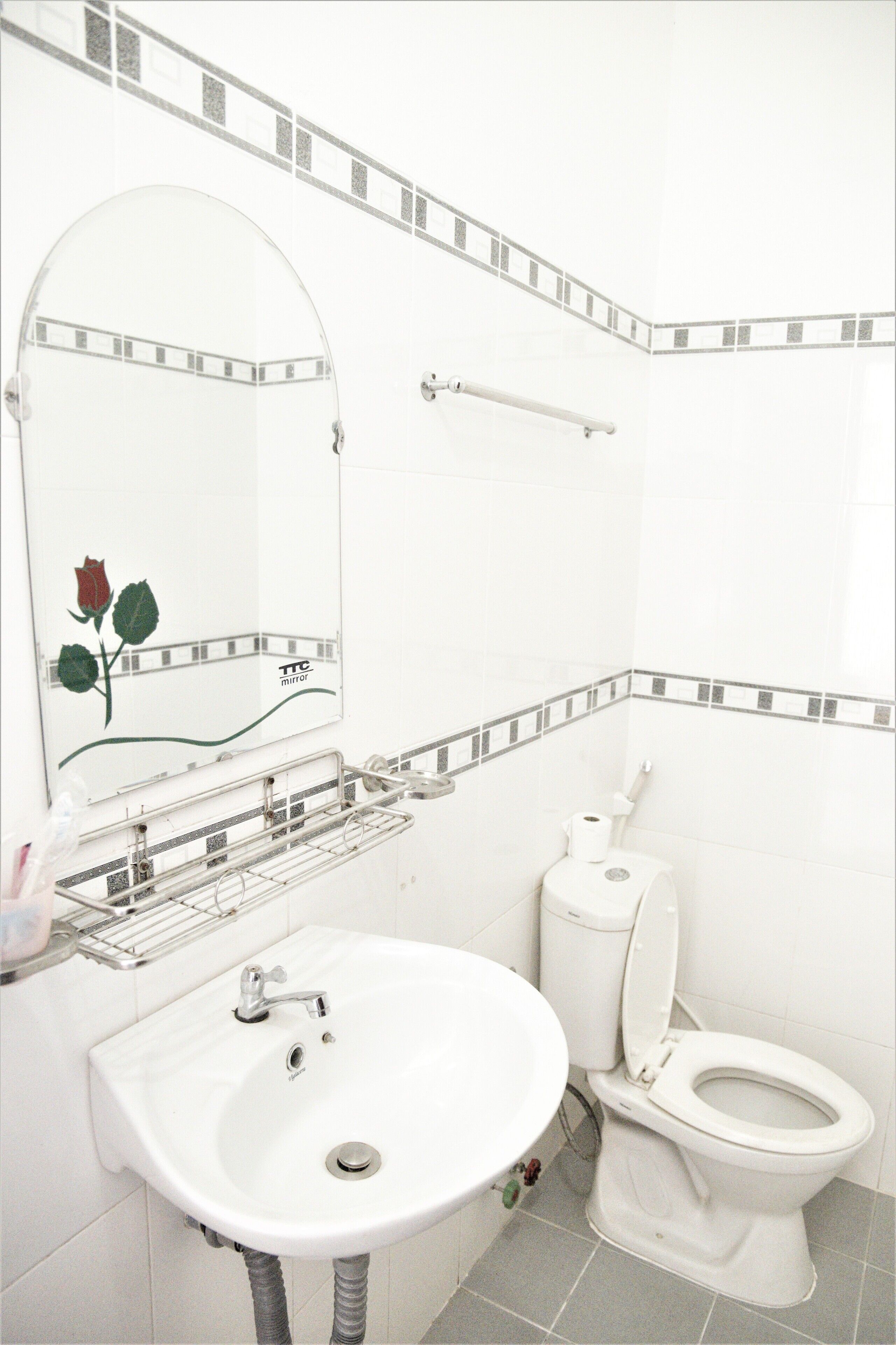 A bathroom with a white sink, a toilet, and a mirror with a rose decoration.