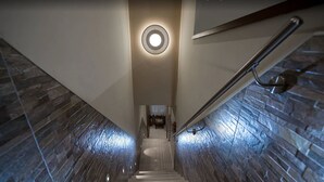 A staircase with stone walls and a handrail, leading to a landing with a circular light fixture. - Hotel Ca Marinella (Venice)