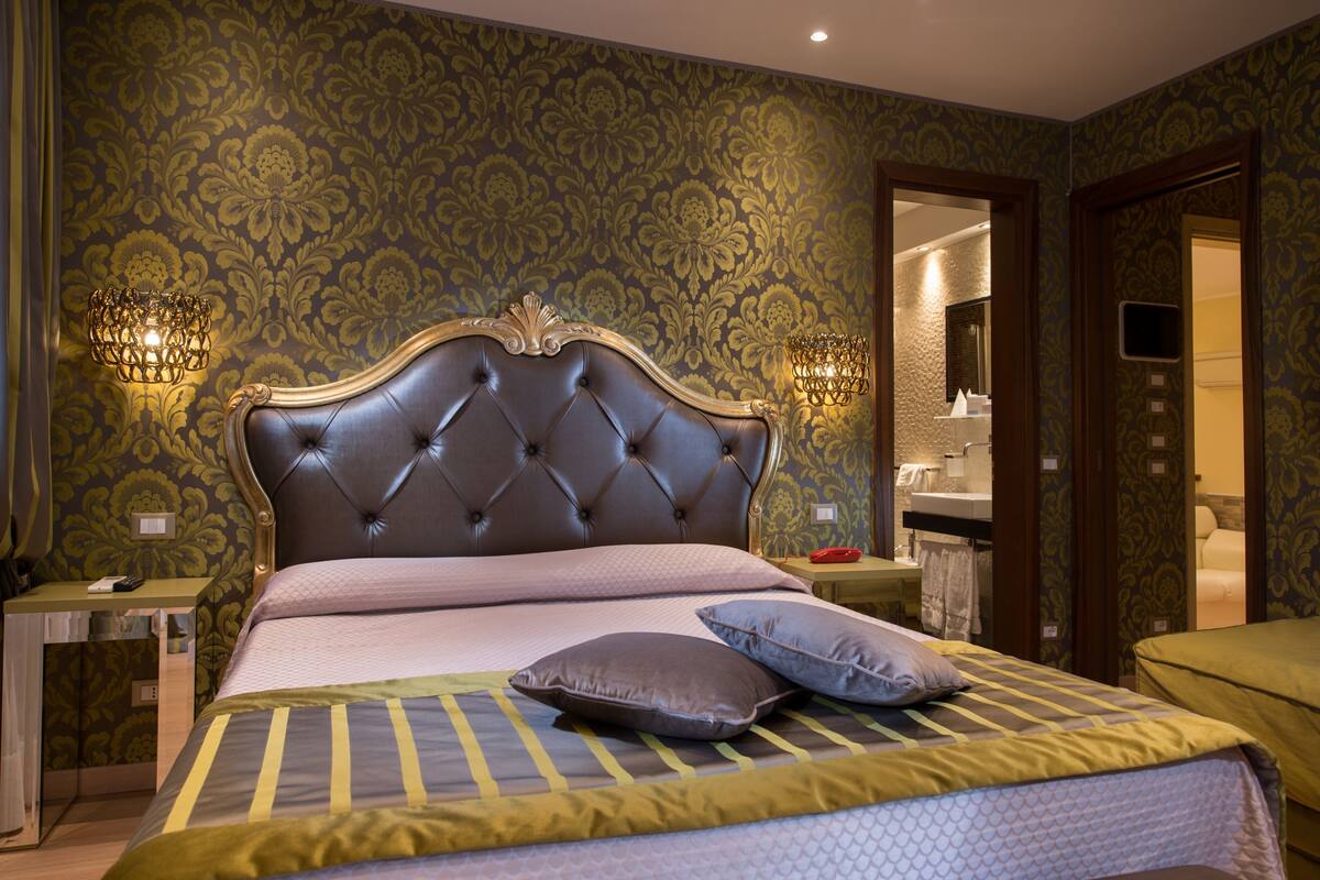 A bedroom with a tufted headboard, a bed with striped bedding, two bedside lamps, and a nightstand with a lamp.