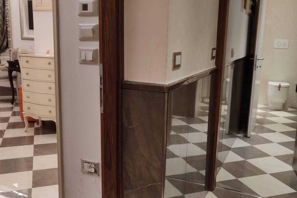 A room with a checkered floor, a wooden door frame, and a mirror reflecting part of the room.