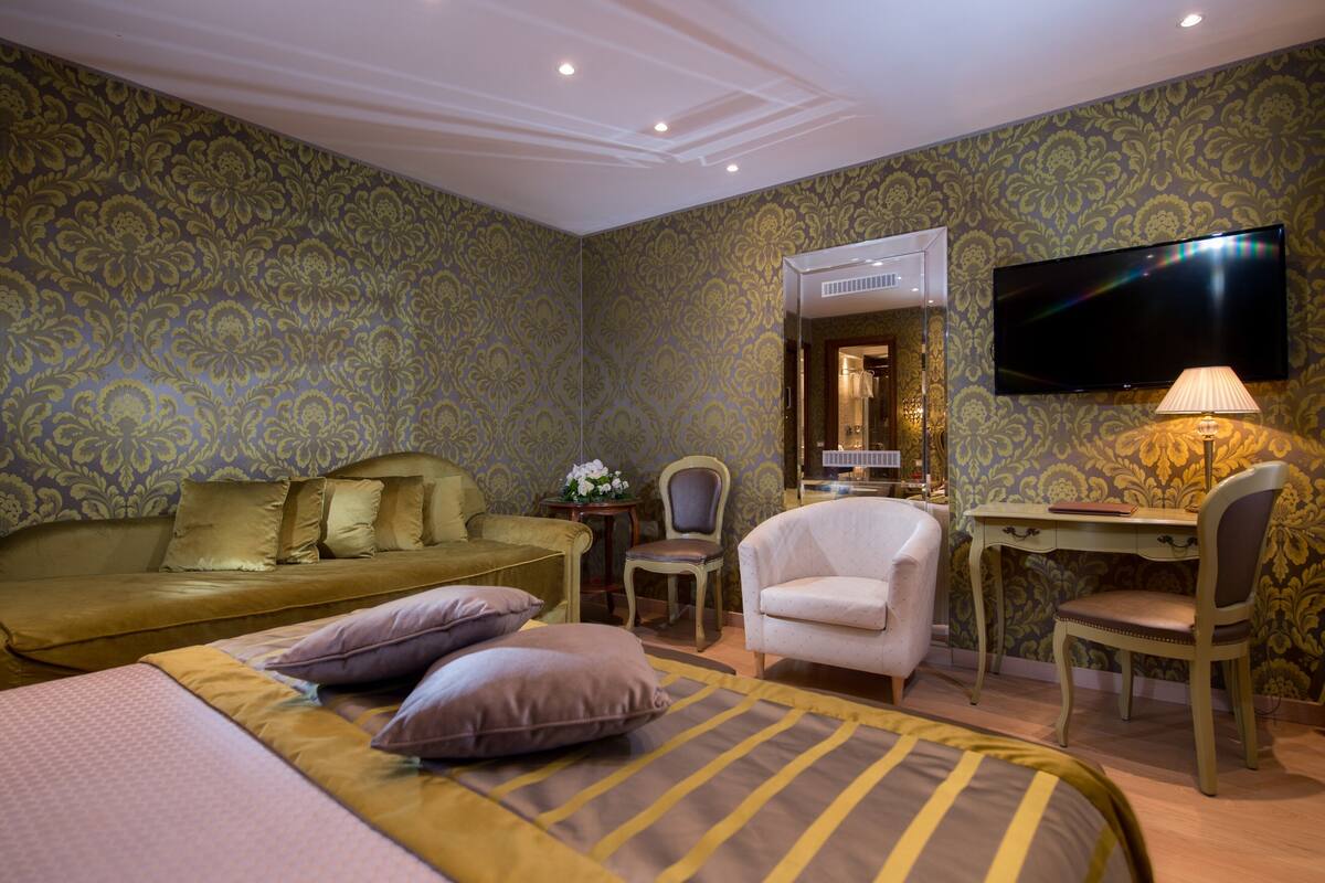 A hotel room with a bed, a desk, a chair, a television, and a mirror.