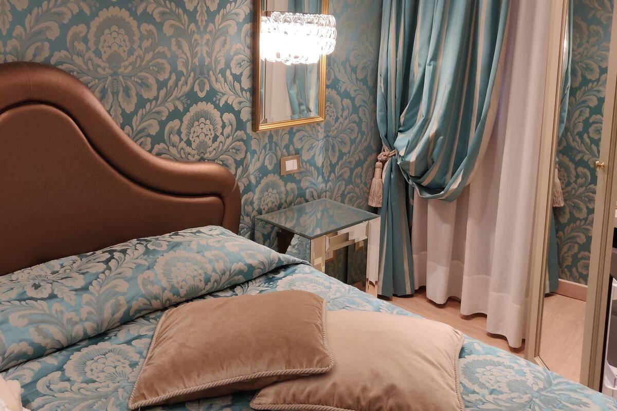 A bedroom with a bed, a nightstand, a mirror, and a window with curtains.