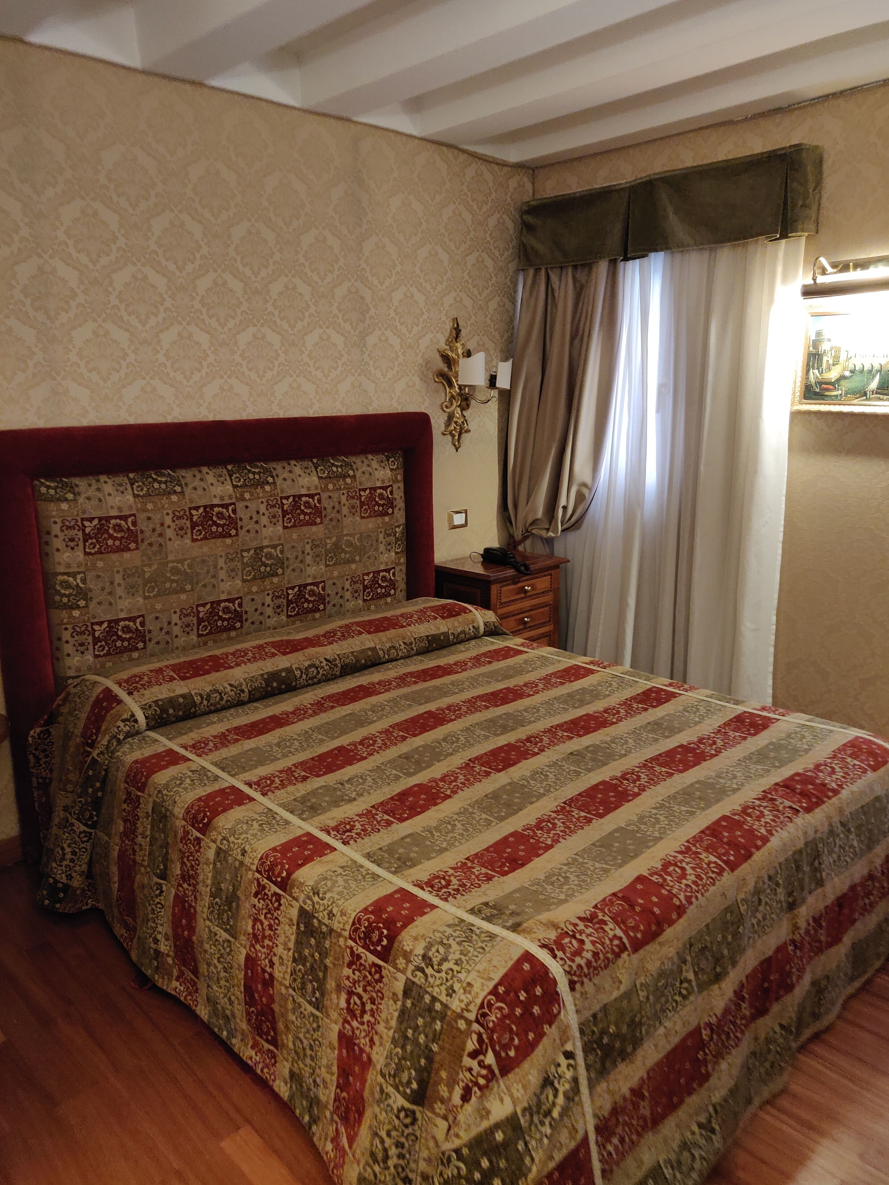 Een slaapkamer met een groot bed, een nachtkastje, een lamp en een raam met gordijnen.