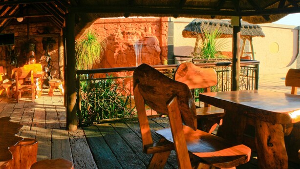 Un interior rústico de madera con techo de paja, mesas y bancos de madera, y una pared de piedra con una cascada.