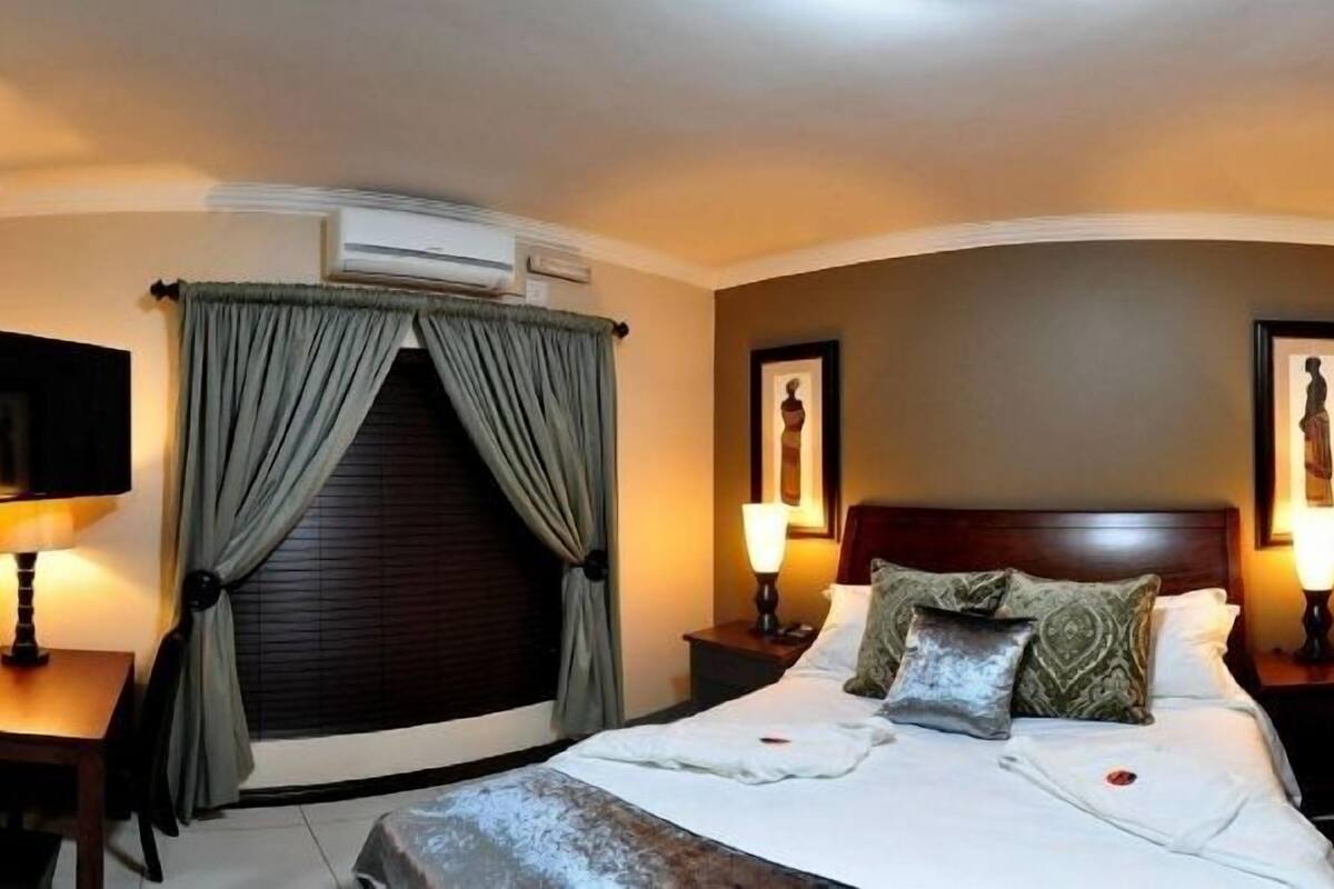 Une chambre d’hôtel équipée d’un lit, de lampes de chevet, d’un bureau, d’une chaise, d’un grand miroir et d’un appareil de climatisation.