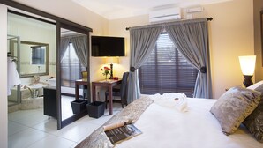Habitación de hotel con cama, escritorio, silla, televisor y baño con espejo y bañera.