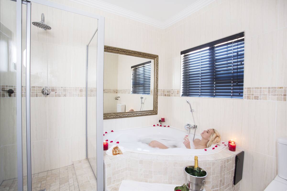 Une salle de bain avec une douche à parois de verre, une baignoire remplie de pétales de roses, des bougies et une bouteille de champagne.
