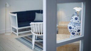 Huoneessa on valkoinen sohva, valkoinen tuoli ja sinivalkoinen maljakko puupöydällä.