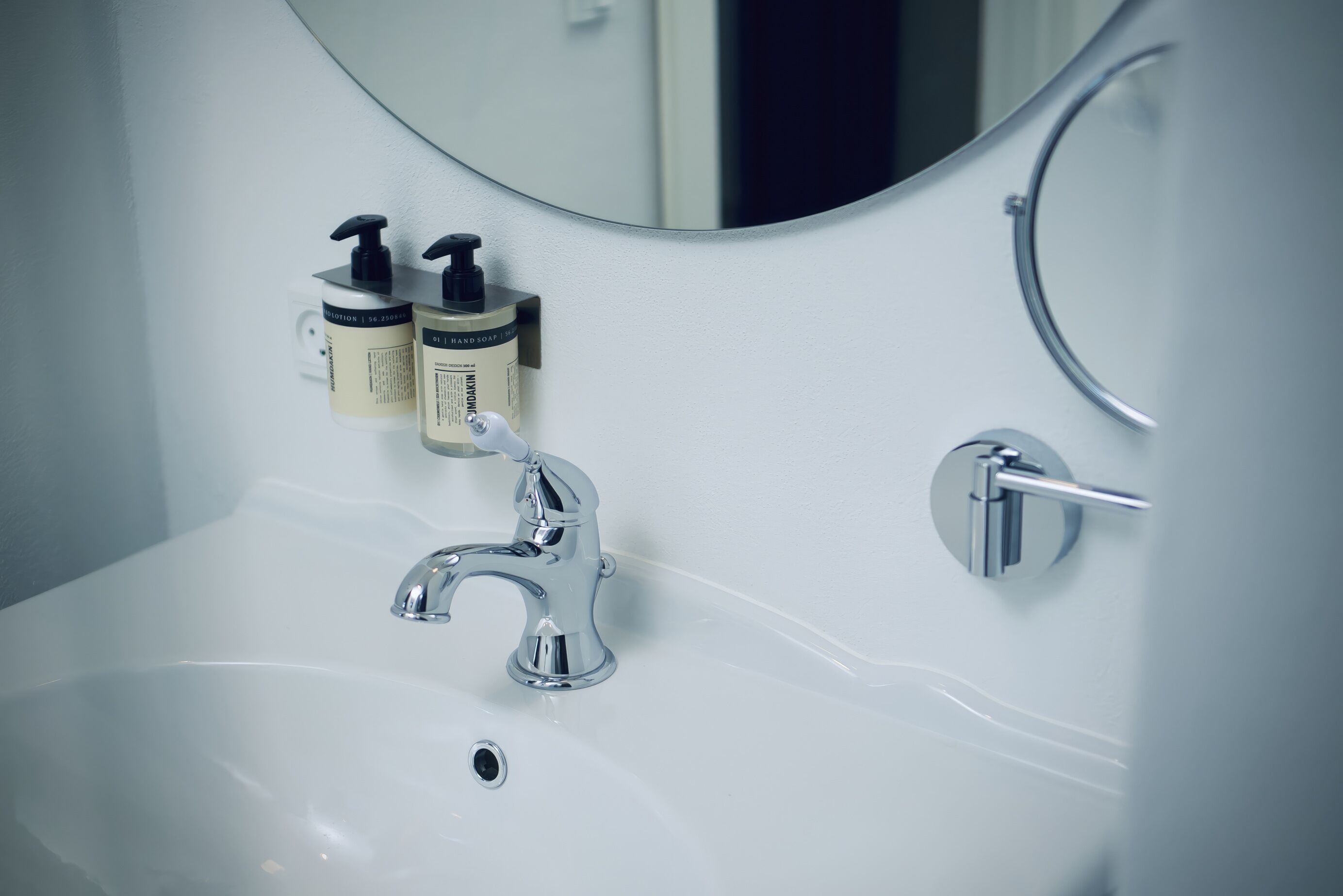 A bathroom sink with a chrome faucet, a mirror, and two hand soap dispensers mounted on the wall.