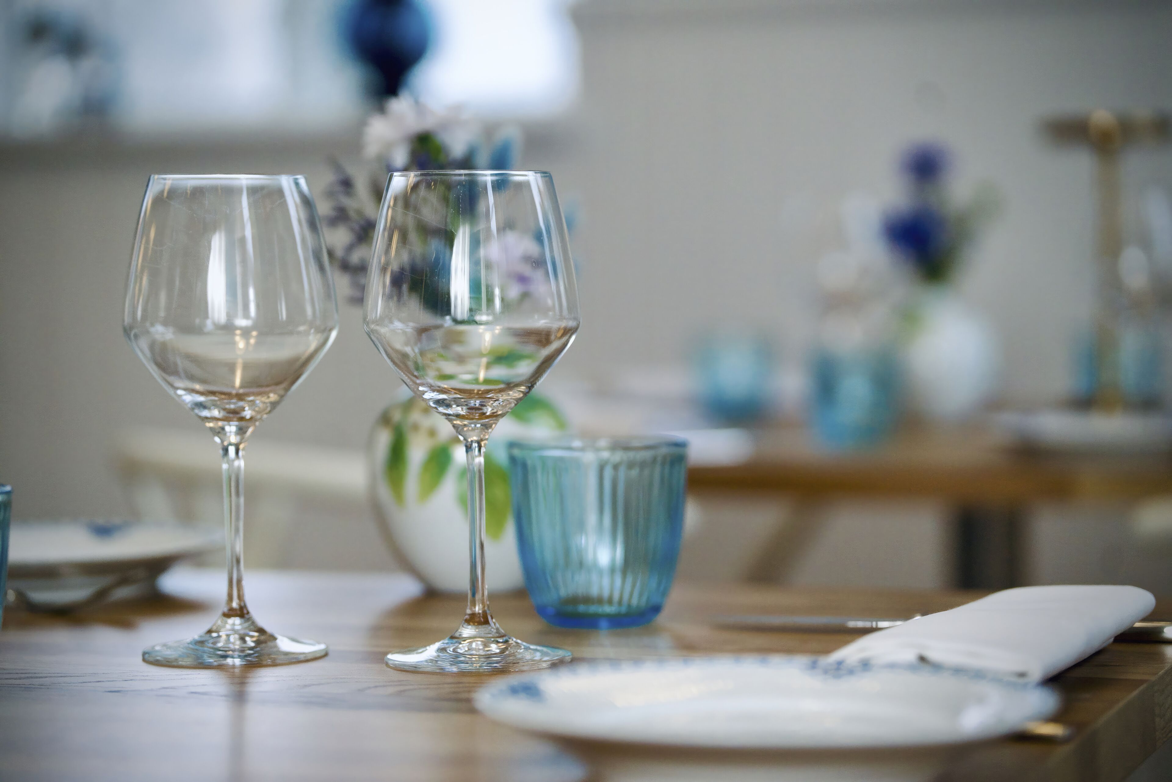 Dos copas de vino vacías sobre una mesa con un vaso azul y un plato blanco con un diseño azulado.